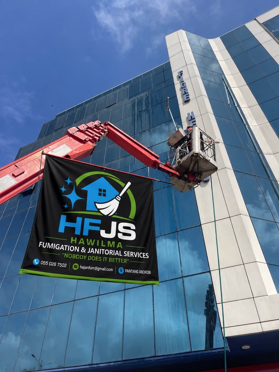 HFJS high-rise team cleaning a glass facade in Accra, with the HFJS banner on the boom lift